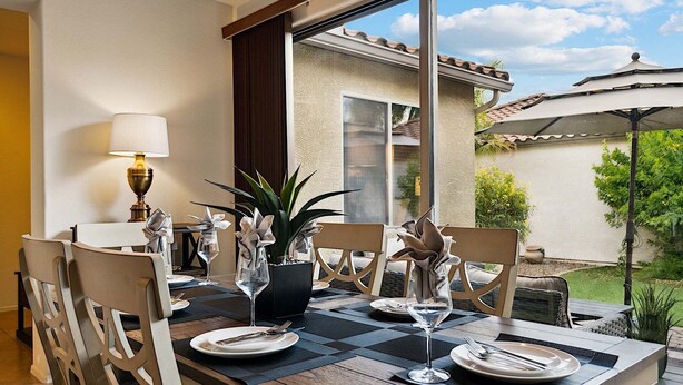 A dining area with a table set for two, featuring a checkered tablecloth, two chairs, a lamp, and potted plants. - Beautifully Furnished Home in Power Ranch ~ Steps away from Community Pool & Spa (Gilbert)