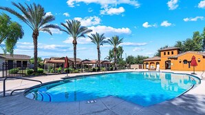 A swimming pool with a clear blue water, surrounded by palm trees and buildings with a Mediterranean architectural style. - Beautifully Furnished Home in Power Ranch ~ Steps away from Community Pool & Spa (Gilbert)