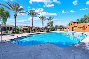 A swimming pool with a clear blue water, surrounded by palm trees and buildings with a Mediterranean architectural style. - Beautifully Furnished Home in Power Ranch ~ Steps away from Community Pool & Spa (Gilbert)