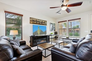 A living room with leather sofas, a fireplace, artwork, and large windows with blinds. - Beautifully Furnished Home in Power Ranch ~ Steps away from Community Pool & Spa (Gilbert)