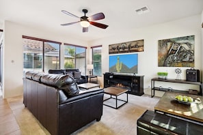 A living room with a leather sofa, a coffee table, a fireplace, and artwork on the walls. - Beautifully Furnished Home in Power Ranch ~ Steps away from Community Pool & Spa (Gilbert)