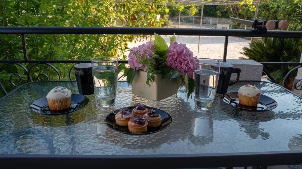 A glass table with a floral centerpiece, two plates of cupcakes, and two black mugs.