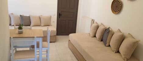 A living room with a beige sofa, a white chair, a wooden table, and a small potted plant.