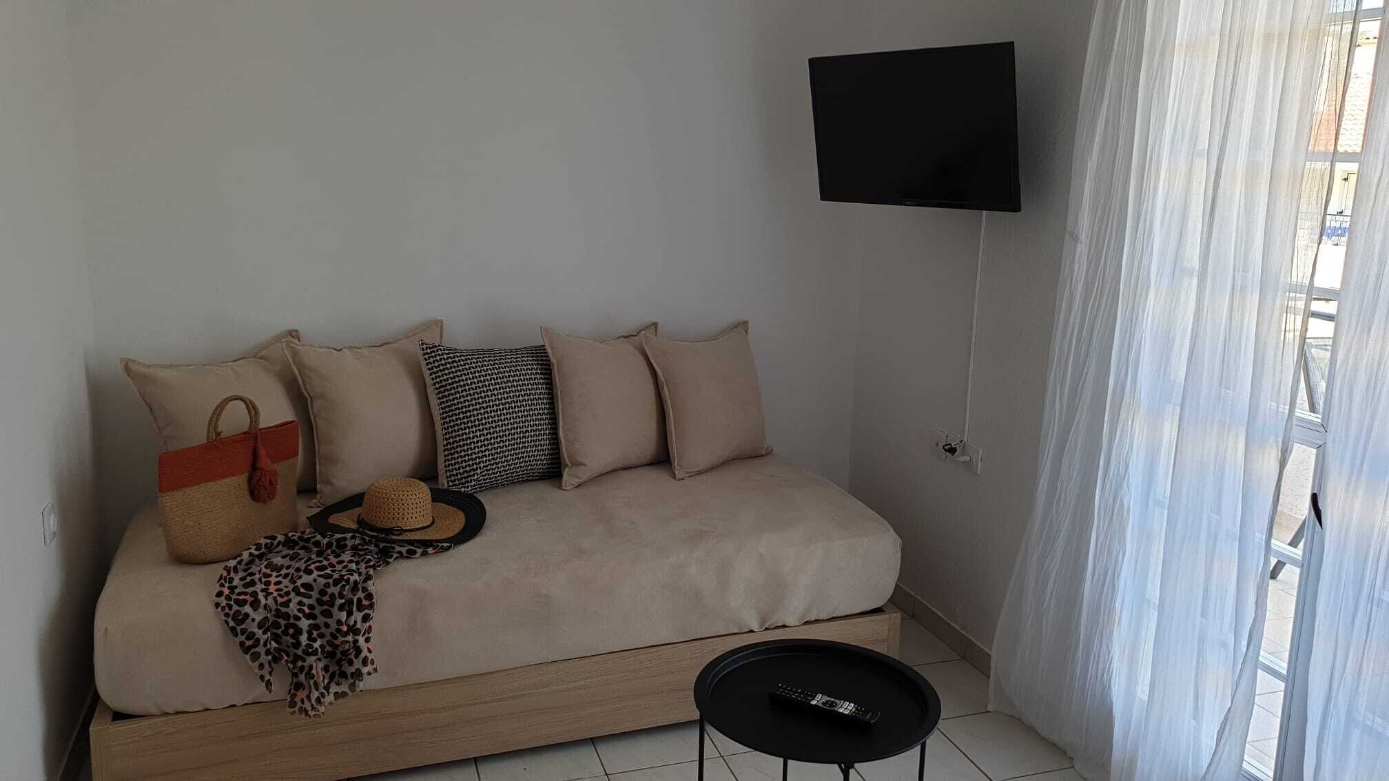 Una sala de estar minimalista con un sofá, un televisor de pantalla plana montado en la pared y una pequeña mesita.