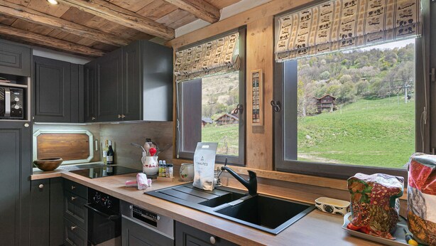 Une cuisine moderne avec des meubles de couleur sombre, une cuisinière noire et une fenêtre agrémentée d’une lambrequin à motifs.