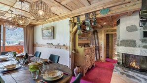 Une salle à manger en bois dotée d’une cheminée, de poutres apparentes en bois au plafond et offrant une vue sur les montagnes.