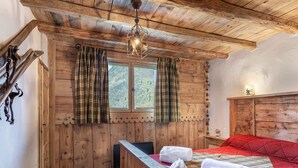 Une pièce de style cabane en bois, avec un lit, une tête de lit en bois, une fenêtre avec des rideaux et un luminaire suspendu.