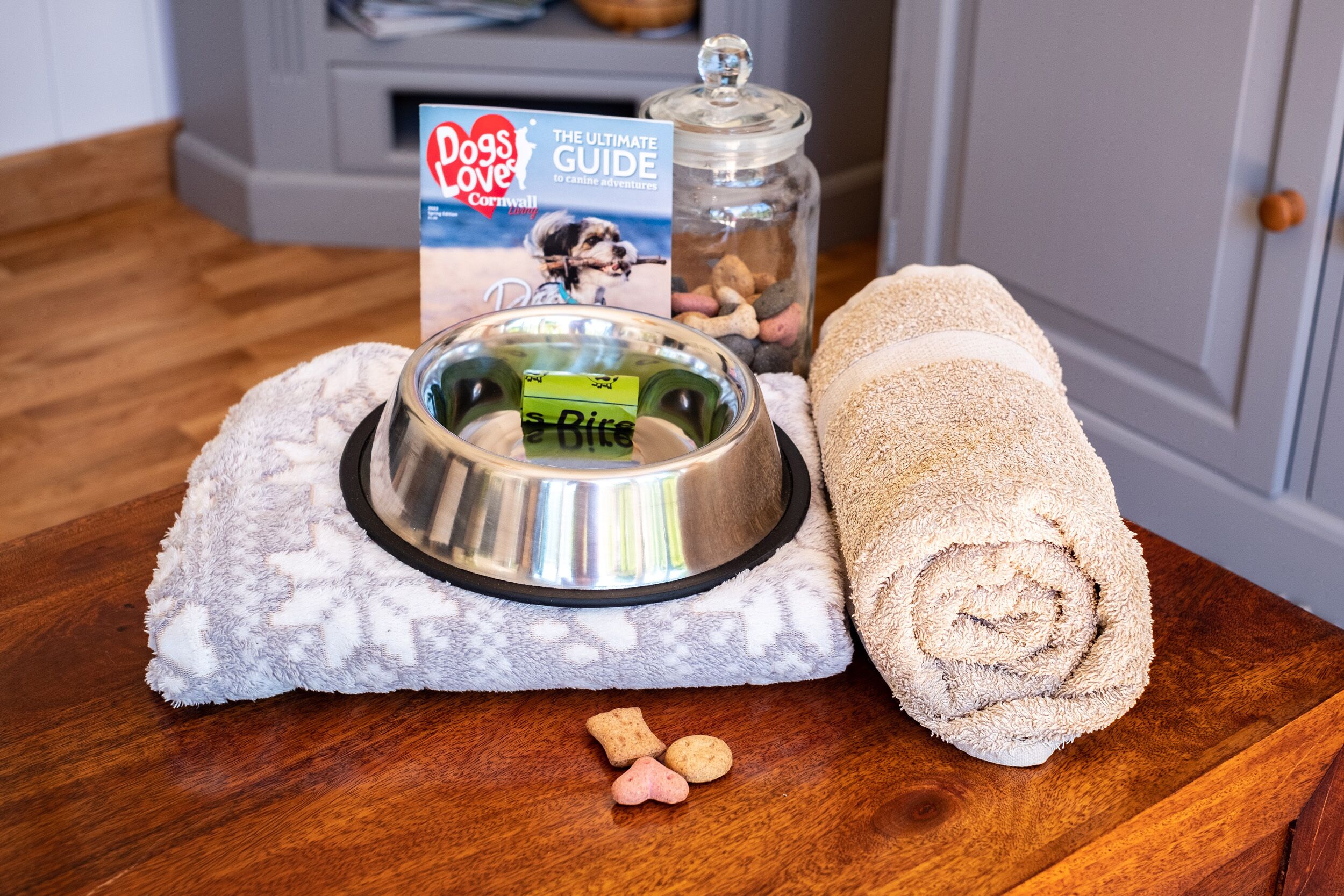 A pet food bowl, a rolled-up towel, and a book on a wooden table.