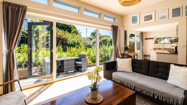 Un salon moderne avec un canapé, une table basse et une vue sur un jardin, grâce à de grandes portes-fenêtres coulissantes.
