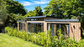Une maison moderne dotée de grandes baies vitrées, entourée d’une végétation luxuriante et d’arbres.