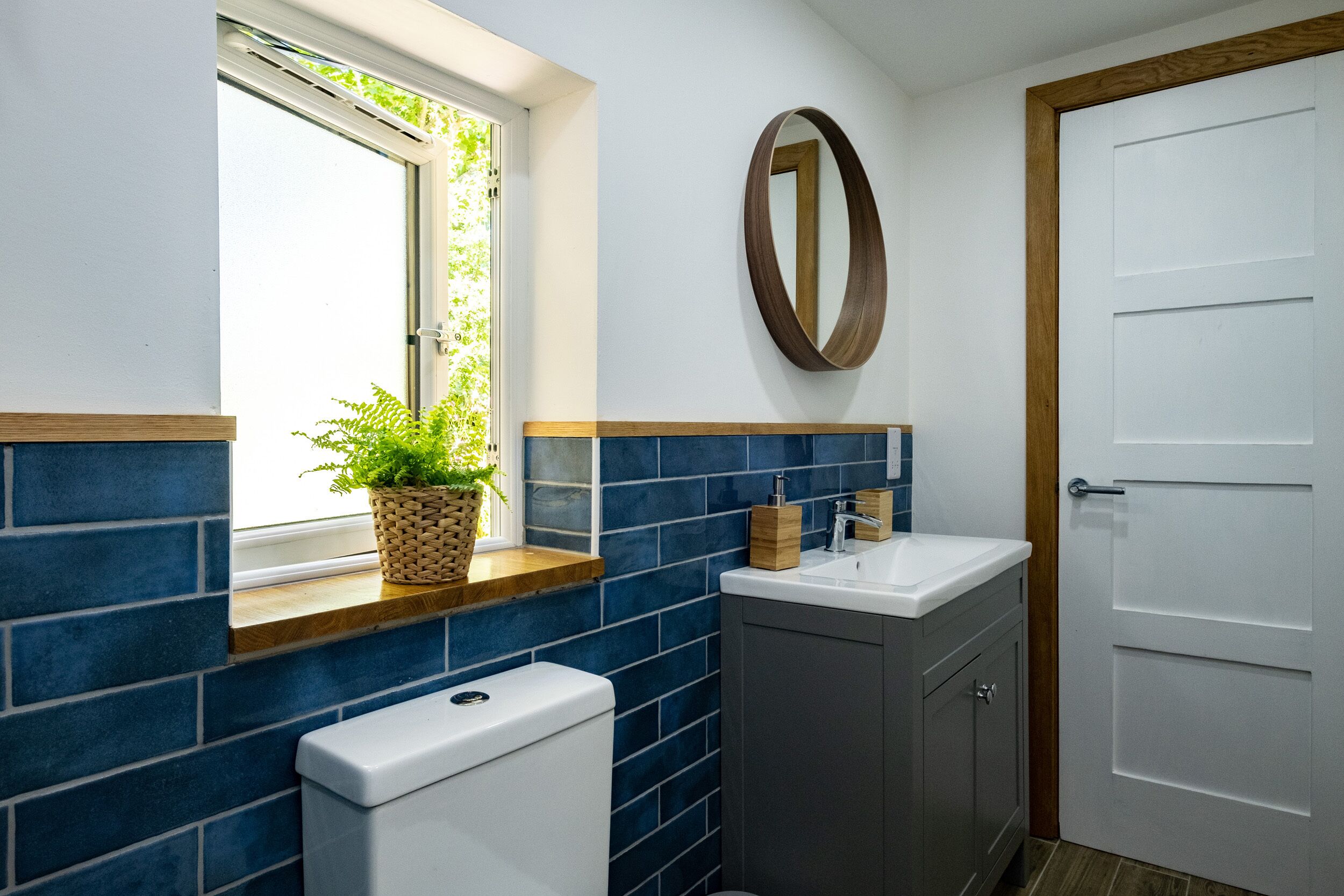 A bathroom with blue tiles, a white toilet, a sink, and a wooden-framed mirror.