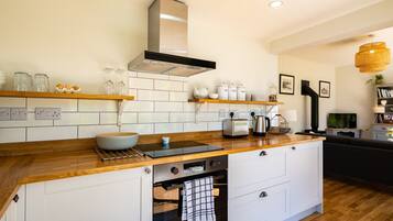 Een moderne keuken met witte kasten, een houten aanrecht en een ingebouwde oven. Op het aanrecht staan planken met glazen potten en een waterkoker.