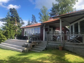 A wooden house with a porch, steps, and a dining area with chairs and a table.