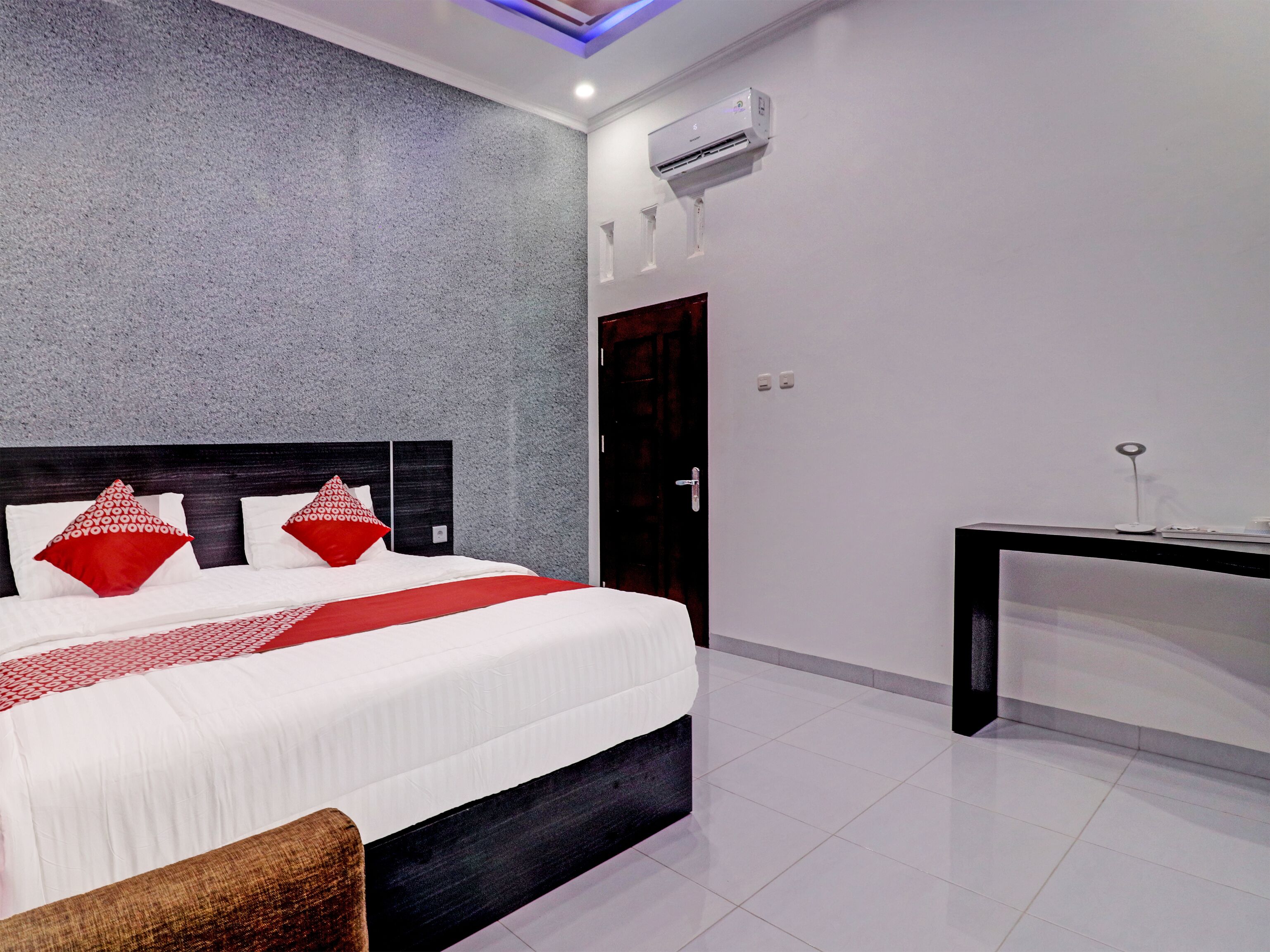 A modern hotel room with a large bed, a dark headboard, and a textured gray wall.
