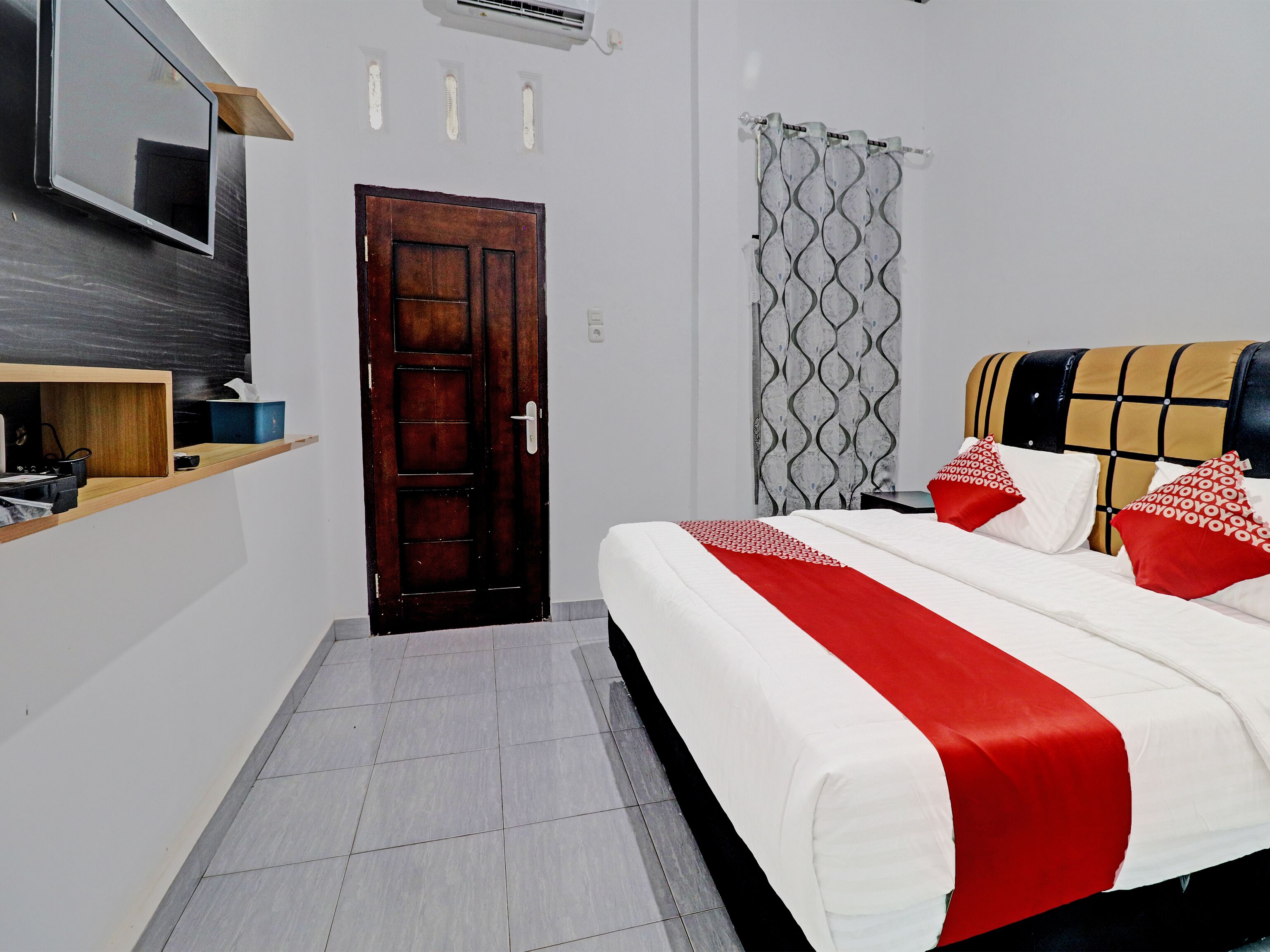 A hotel room with a bed, a wooden shelf, a door, and a curtain.