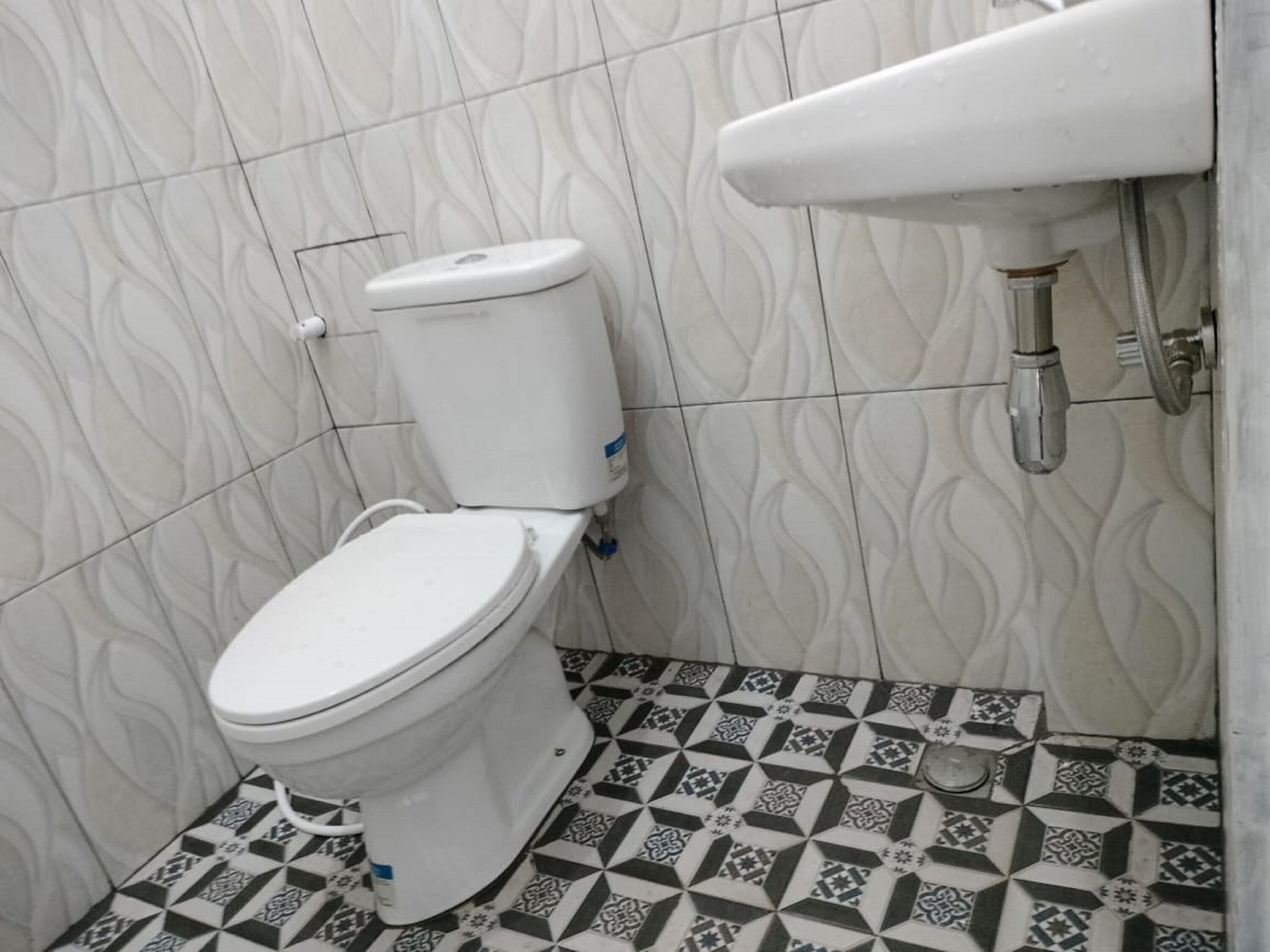 A bathroom with a toilet, a sink, and patterned floor tiles.