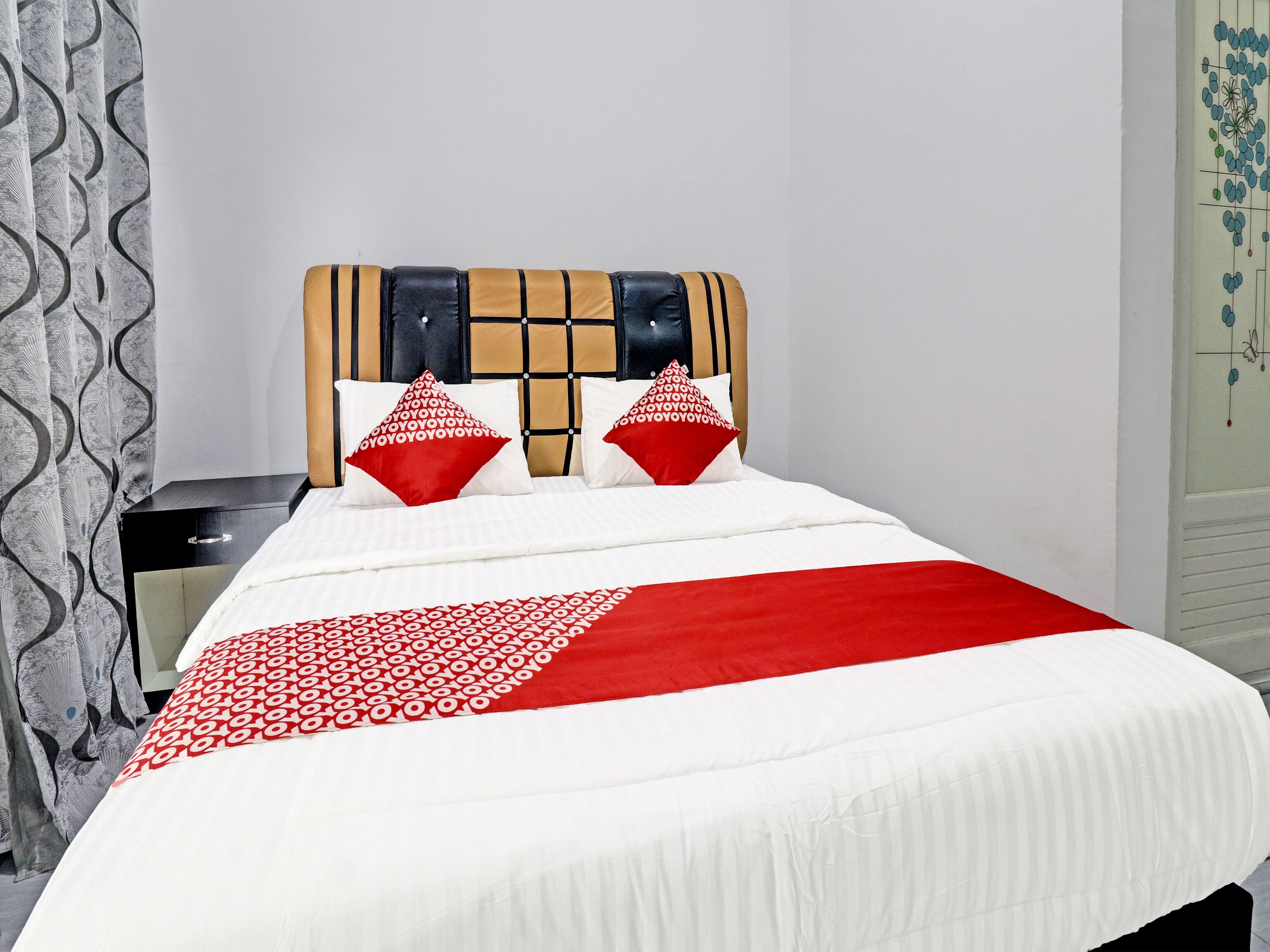 Ein Bett mit einem gemusterten Überwurf, zwei roten Kissen und einem Kopfteil mit geometrischem Muster.