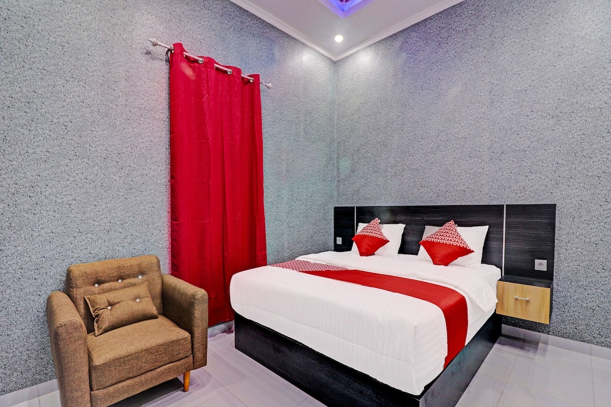 Una habitación de hotel moderna con una cama grande, un sillón marrón y una cortina roja.