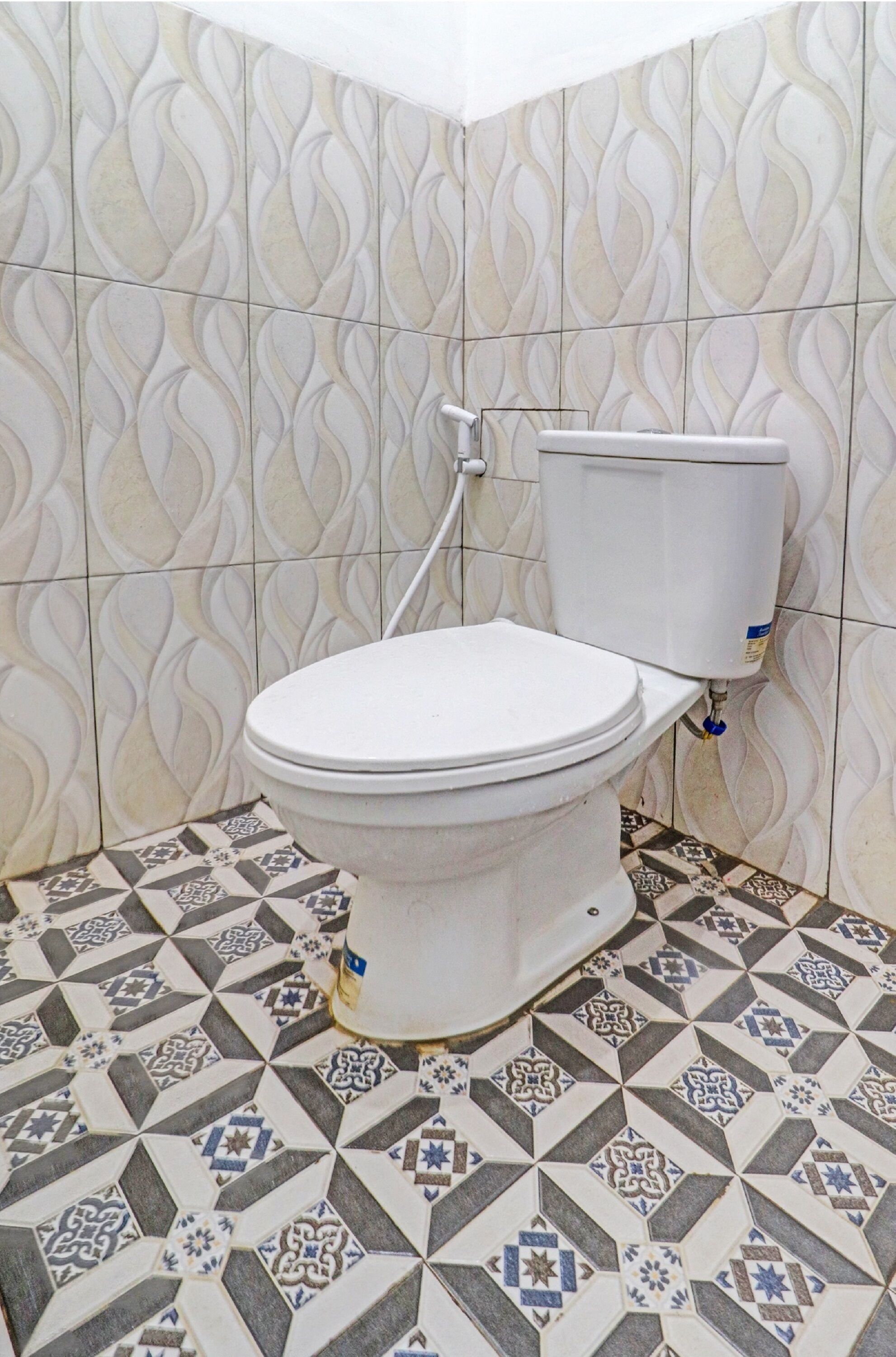 A bathroom with a toilet, patterned tiles on the walls and floor, and a visible plumbing fixture.