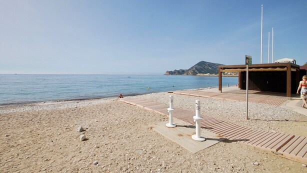 A beach with a wooden deck, white bollards, and a small shelter.