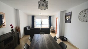 A dining area with a wooden table and chairs, a sofa, a small cabinet, and a pendant light.