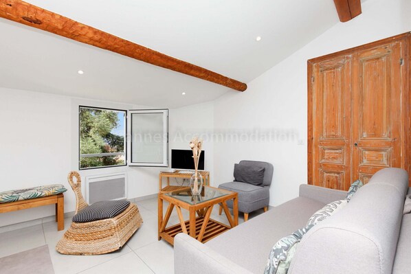 A modern living room with a sofa, a wicker chair, a glass-top coffee table, a grey armchair, and a wooden wardrobe. - Bronze-2525-Lovely renovated apartment (Cannes)