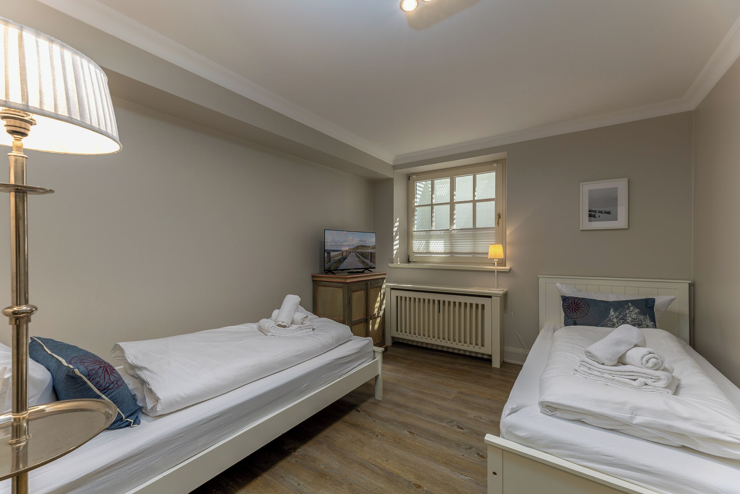A bedroom with two single beds, a radiator, a TV, and a lamp.