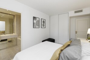 A hotel room with a bed, a bedside table with a lamp, a mirror, and two framed pictures on the wall.