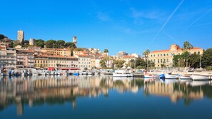 Uma vila costeira com edifícios históricos, uma marina com barcos e uma torre do relógio imponente.