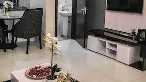 Un salon moderne avec un téléviseur, des meubles aux couleurs noir et blanc, et un coin repas comprenant une chaise et une table.