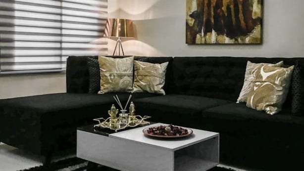 Un salon moderne avec un canapé noir, une table basse blanche et un tableau accroché au mur.