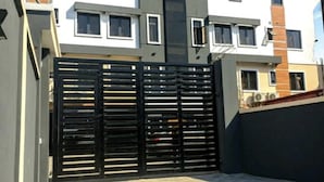 Un bâtiment moderne à deux étages, doté d’un portail en métal noir, d’une allée pavée et surplombé d’un ciel bleu clair.