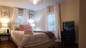 A neatly arranged bedroom with a bed, bedside tables, a dresser, and a television.