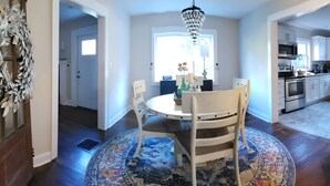 A dining area with a round table, chairs, a chandelier, and a patterned rug.