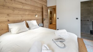 Quarto moderno com cabeceira de madeira, cama grande com roupa de cama branca, um par de chinelos e um closet espaçoso.