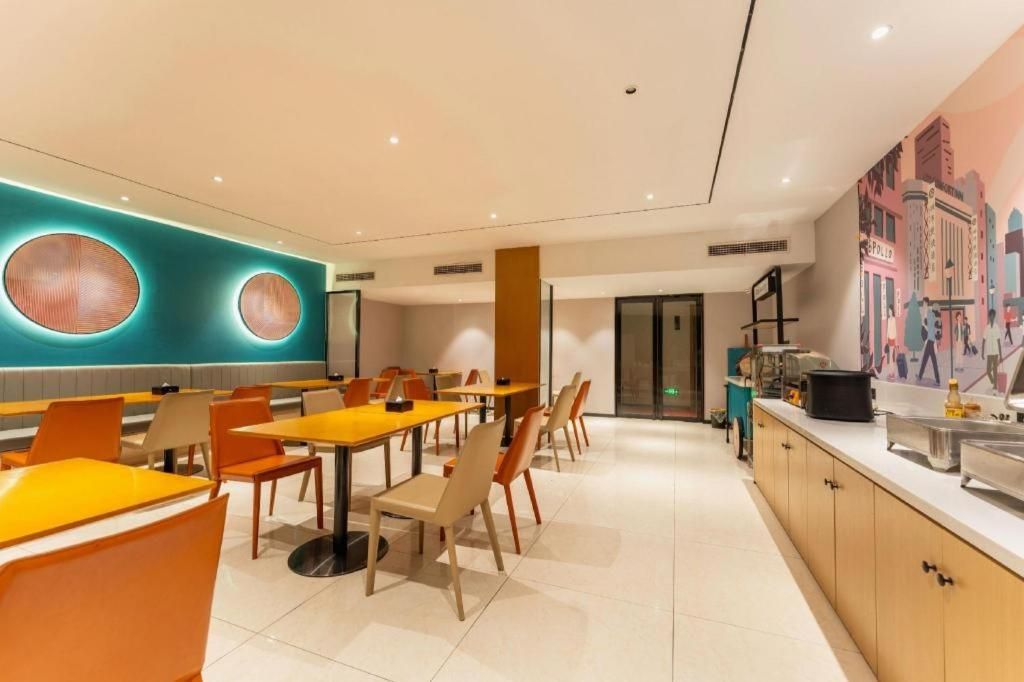 Un comedor moderno con mesas y sillas redondas, una encimera de cocina con electrodomésticos y un mural en la pared.