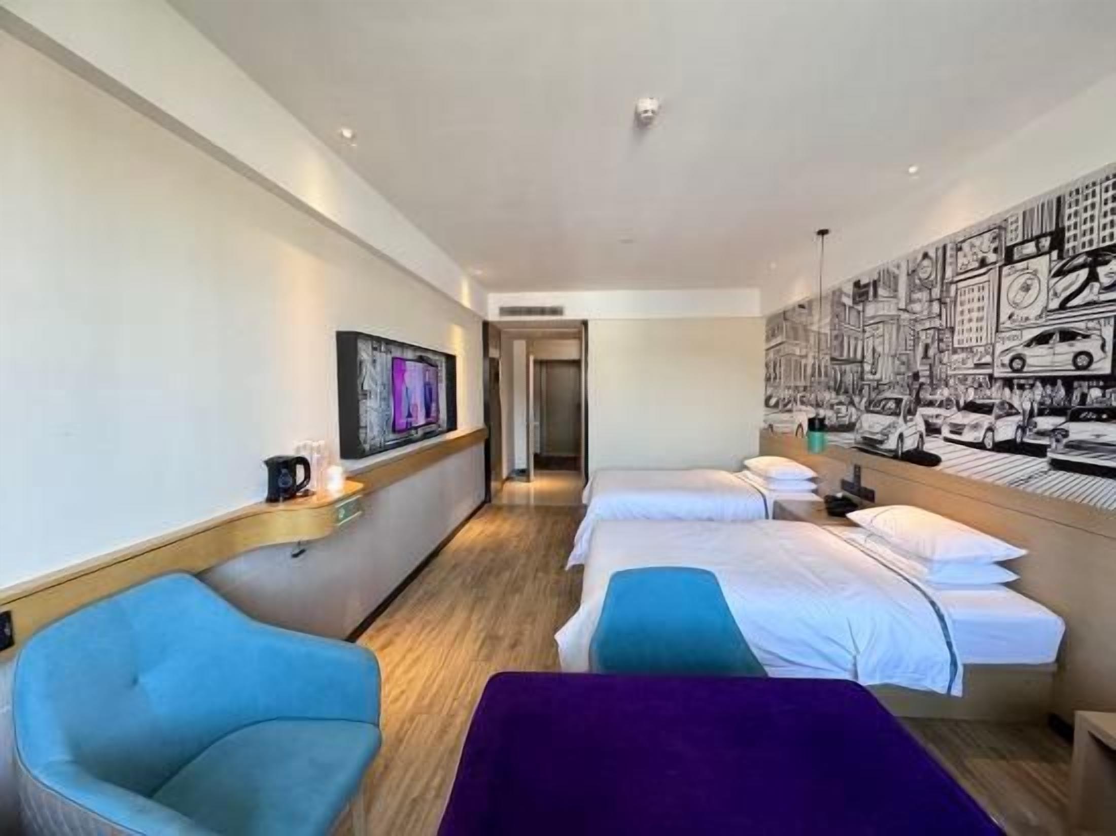 Habitación de hotel con dos camas, una zona de estar y un mural urbano en la pared.
