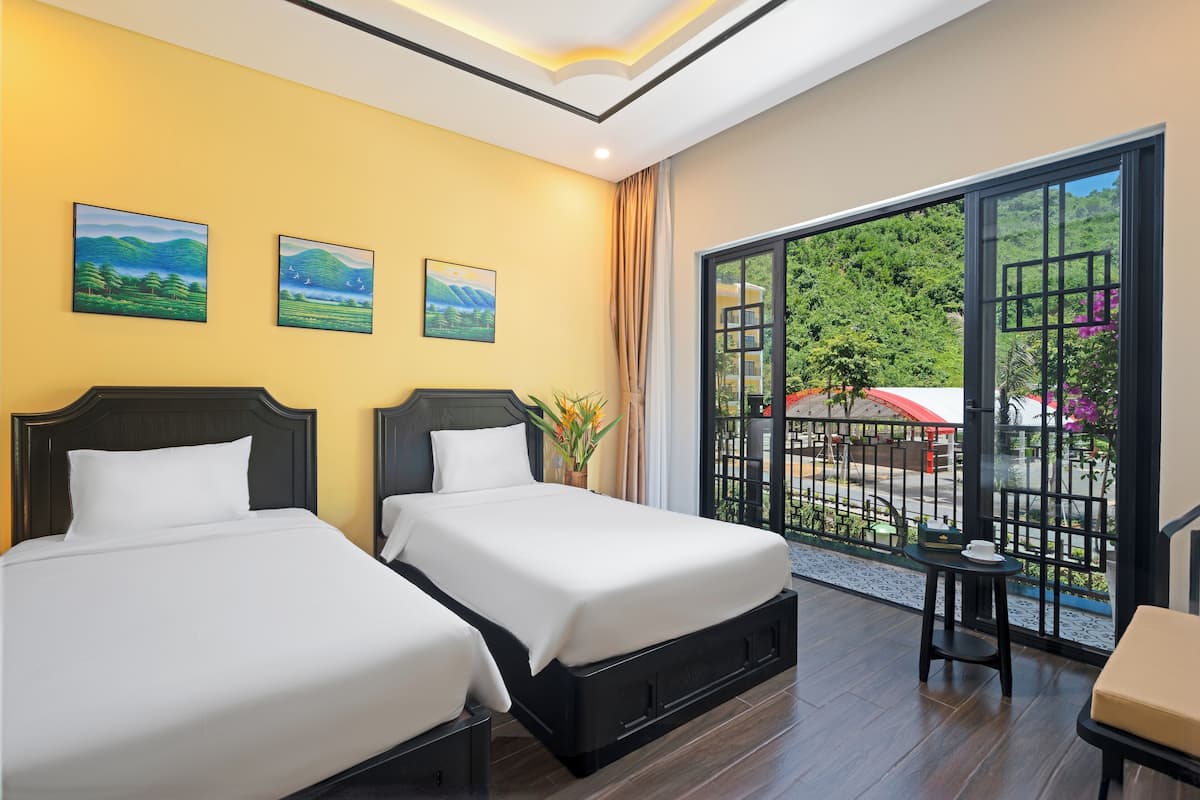 Une chambre d’hôtel avec deux lits, un balcon donnant sur un espace verdoyant et une table avec une chaise.