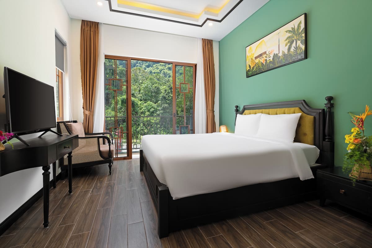 Une chambre d’hôtel avec un grand lit, un bureau avec une télévision, une chaise et une vue sur la verdure par la fenêtre.