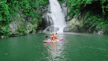 Two people kayaking on a river with a waterfall in the background.