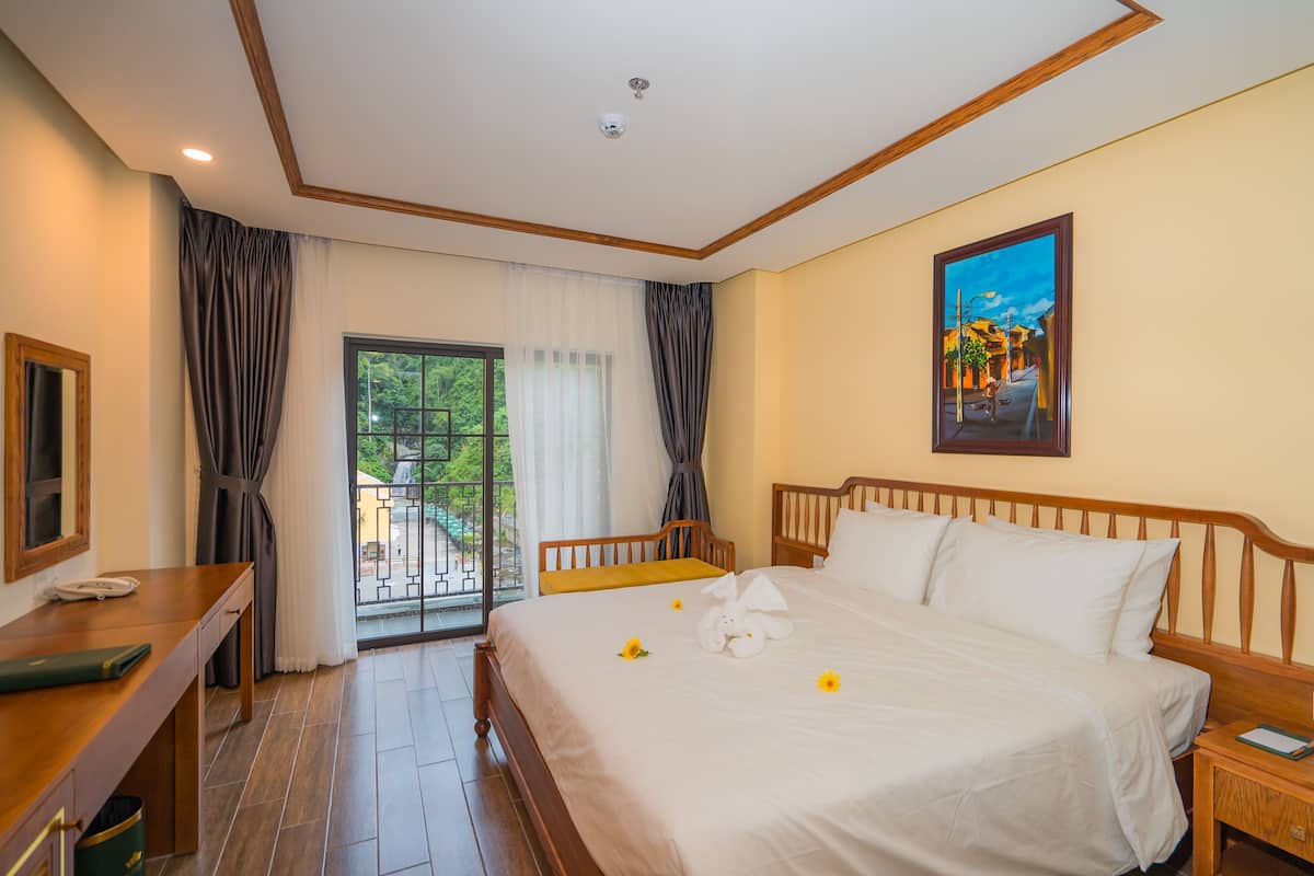 Une chambre d’hôtel avec un lit, un bureau, une chaise, une fenêtre avec des rideaux et un tableau au mur.