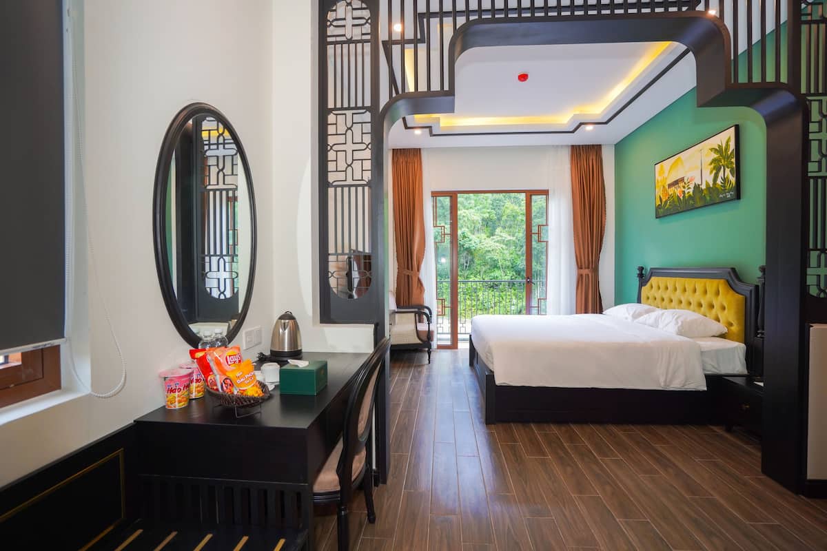 Une chambre d’hôtel avec un lit, un bureau doté d’un miroir, une commode et une vue sur la verdure.