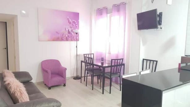 A living room with a sofa, a chair, a dining table with chairs, a flat-screen TV mounted on the wall, and a window with curtains. - Slaughterhouse Madrid 1 (Madrid)