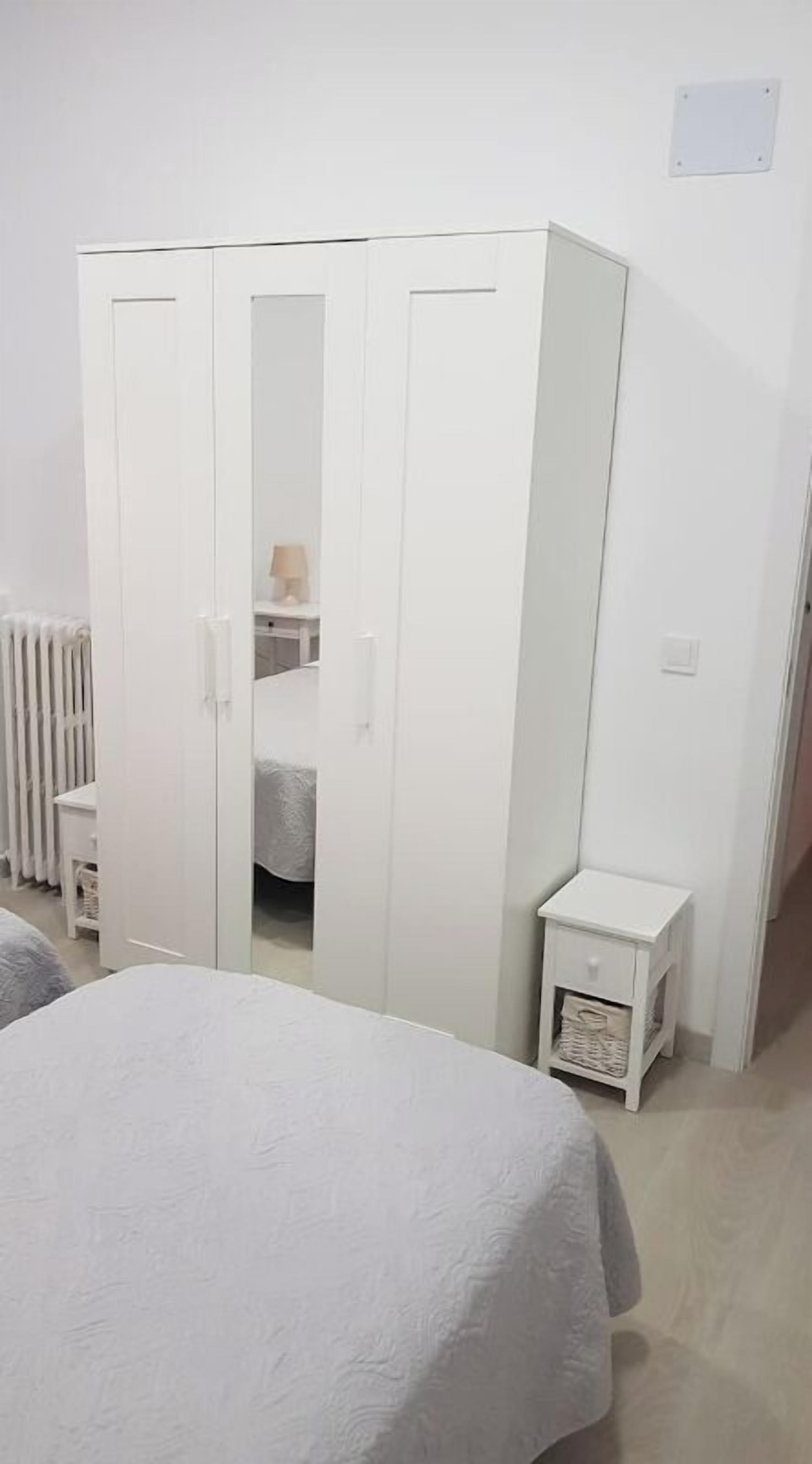 Une chambre à coucher avec une armoire blanche, une table de chevet et un radiateur.