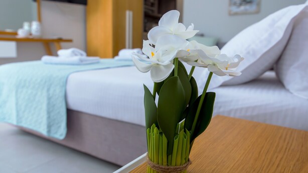 A bed with white bedding and a wooden nightstand with a vase of white flowers. - Olea Garden Rooms (Volvi)