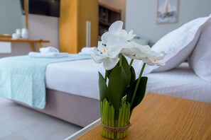 A bed with white bedding and a wooden nightstand with a vase of white flowers. - Olea Garden Rooms (Volvi)
