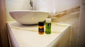 A bathroom with a white marble sink, a bottle of Karavaki shower gel, and a bottle of skin essentials hairshampoo. - Olea Garden Rooms (Volvi)
