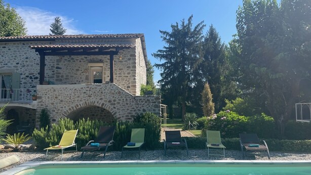 Un edificio de piedra con piscina y sillones de descanso.