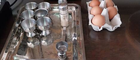 Uma bancada de cozinha com uma bandeja de aço inoxidável contendo diversos utensílios, um cozido lento e uma embalagem de ovos.