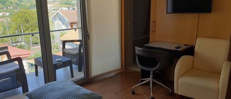 Ein Zimmer mit Balkon, Schreibtisch, Stuhl und Bett.